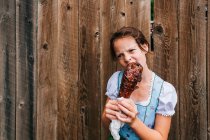 Menina em pé por uma cerca comendo uma perna de peru grelhado, EUA — Fotografia de Stock