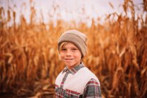 Garoto sorridente de pé em um campo de milho no outono, EUA — Fotografia de Stock