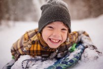 Porträt eines lächelnden Jungen, der auf einem Schlitten im Schnee liegt, Wisconsin, USA — Stockfoto
