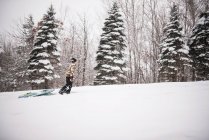 Chico tirando de un trineo en una colina en la nieve, Wisconsin, EE.UU. - foto de stock