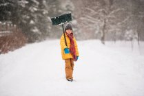 Niño con una pala de pie en la nieve en un largo camino cubierto de nieve, Wisconsin, EE.UU. - foto de stock