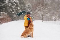 Garçon avec une pelle debout avec son chien dans la neige sur une longue allée couverte de neige, Wisconsin, États-Unis — Photo de stock