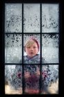 Мальчик смотрит в морозное окно, США — стоковое фото