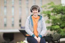 Lächelnde Frau sitzt draußen und hört Musik, Deutschland — Stockfoto