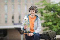 Mujer sonriente sosteniendo una flor, sentada al aire libre escuchando música, Alemania - foto de stock