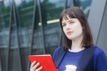 Portrait d'une femme souriante debout à l'extérieur tenant une tablette numérique et une tasse de café, Allemagne — Photo de stock