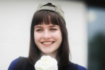Retrato de una mujer sonriente con una gorra de béisbol sosteniendo una flor, Alemania - foto de stock