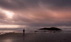 Frau steht bei Sonnenuntergang während eines Sturms am Strand, Kanada — Stockfoto