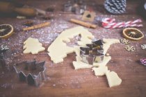 Тесто для печенья, ножи для печенья и рождественские украшения на деревянном столе — стоковое фото