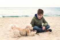 Хлопчик, який тримає палицю, граючи зі своїм собакою на пляжі (Болгарія). — стокове фото
