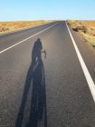 Shadow of a cyclist on a straight road, Lanzarote, Canary Islands, Spain — Stock Photo