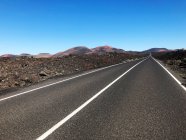 Straight road through volcanic terrain, Timanfaya, Lanzarote, Canary Islands, Spain — Stock Photo