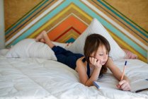 Retrato de una chica acostada en su cama haciendo sus deberes - foto de stock