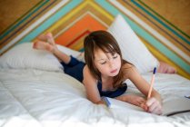 Ritratto di una ragazza sdraiata sul letto a fare i compiti — Foto stock