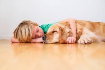 Мальчик лежит на полу обнимая золотую собаку-ретривер — стоковое фото