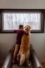 Girl and a golden retriever standing on an armchair looking out of a window — Stock Photo
