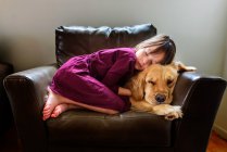 Girl curled up in an armchair with a golden retriever dog — Stock Photo