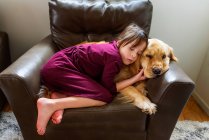 Girl curled up in an armchair with a golden retriever dog — Stock Photo