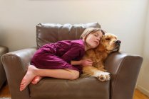 Fille enroulée dans un fauteuil avec un chien golden retriever — Photo de stock