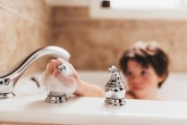 Garçon dans un bain moussant éteindre le robinet — Photo de stock