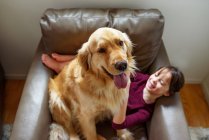 Happy girl sitting in an armchair with a golden retriever dog — Stock Photo