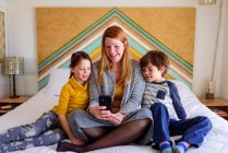Mãe e crianças olhando para o smartphone juntos na cama — Fotografia de Stock