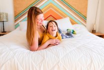 Portrait of a mother and daughter lying on a bed talking — Stock Photo