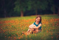 Happy girl sitting in a meadow with wildflowers laughing, USA — Stock Photo