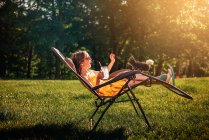 Happy girl sitting in the garden with a chicken on her chair — Stock Photo