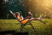Glückliches Mädchen sitzt im Garten mit einem Huhn auf ihrem Stuhl — Stockfoto