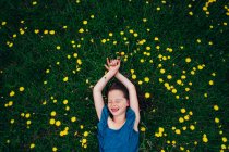 Над головою відкривається вид на щасливу дівчину, яка лежить на лузі з польовими квітами (США). — стокове фото