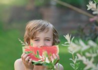 Sonriente niño de pie en el jardín sosteniendo una rebanada de sandía, Bedford, Halifax, Nueva Escocia, Canadá - foto de stock