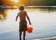 Niño de pie en un lago sosteniendo un cubo, Bedford, Halifax, Nueva Escocia, Canadá - foto de stock