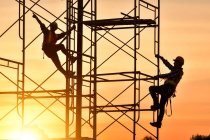 Silhouette of two construction workers climbing scaffolding on a construction site, Thailand — Stock Photo