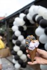 Mano umana con un cono di gelato al sesamo nero e viola — Foto stock