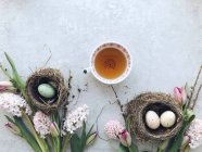 Easter eggs in nests with flowers and tea — Stock Photo