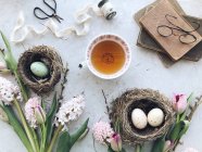 Œufs de Pâques dans des nids avec thé, fleurs et livres — Photo de stock