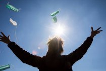 Vista trasera de una mujer de pie al aire libre lanzando máscaras en el aire - foto de stock