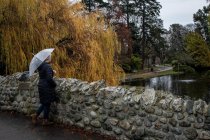 Woman standing on a stone bridge holding an umbrella, Beacon Hill Park, Victoria, British Columbia, Canada — Stock Photo