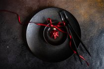 Minimalistic table setting with black ceramic plate and festive decor on concrete background — Stock Photo