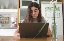 Дівчина-підліток сидить на кухні за допомогою ноутбука — стокове фото