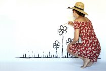 Woman painting flowers in a white wall — Stock Photo