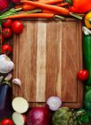 Planche à découper en bois entourée de fruits et légumes frais — Photo de stock