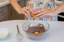 Woman adding eggs to a chocolate cake mixture — Stock Photo