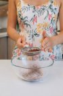 Femme debout dans la cuisine tamisant la poudre de cacao dans un bol de farine — Photo de stock