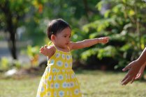 Portrait of a girl in a garden walking towards outstretched arms, Indonesia — Stock Photo