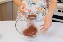 Женщина, стоящая на кухне, просеивает порошок какао в миску муки — стоковое фото