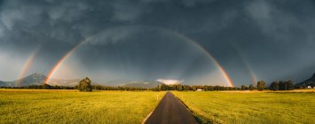 Doppelter Regenbogen über einer Straße durch ländliche Landschaft, Salzburg, Österreich — Stockfoto