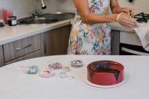 Woman standing in a kitchen decorating a chocolate red velvet cake — Stock Photo