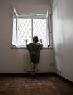 Visão traseira de uma menina presa em uma sala olhando através da janela — Fotografia de Stock